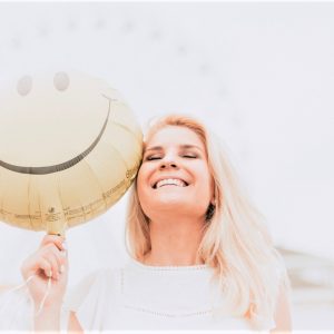 woman smiling while holding happy face balloon